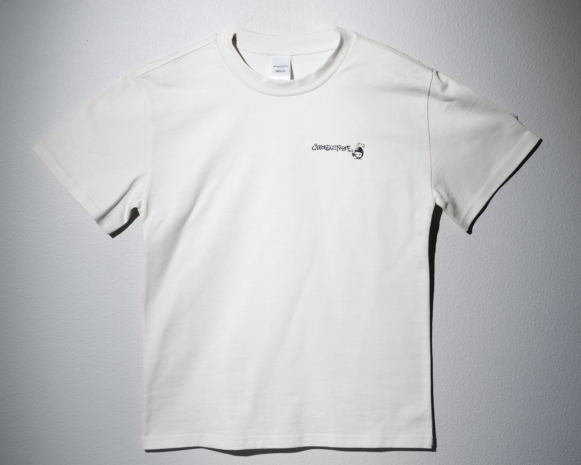 a heavyweight tee in white with a left chest graphic of the second to none logo in graffiti type